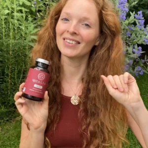 Redhead girl sitting in a garden and holding a bottle of Qualia Skin in her right hand