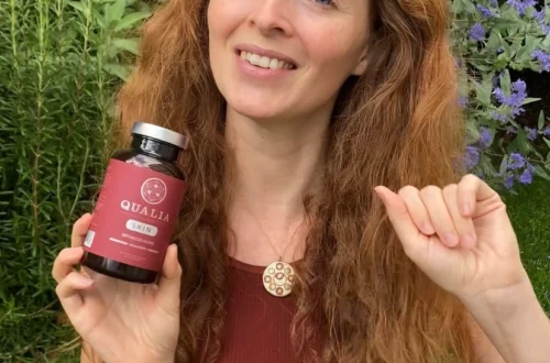 Redhead girl sitting in a garden and holding a bottle of Qualia Skin in her right hand